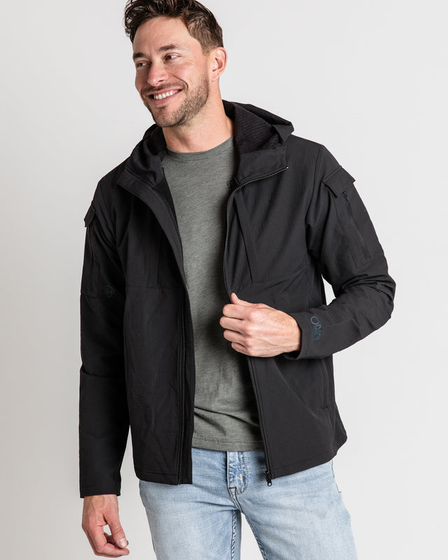 A person wearing a black ODIN Disc Golf jacket with a hood, showcasing the front disc marker pocket.