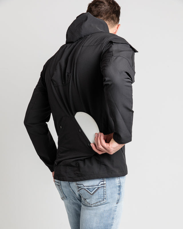 A person wearing a black ODIN Disc Golf jacket with a hood, showcasing the back lower pocket designed for disc storage.