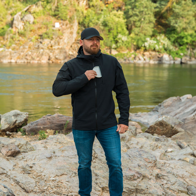 A person wearing a black ODIN Disc Golf jacket with a hood, showcasing inserting the front disc marker pocket.