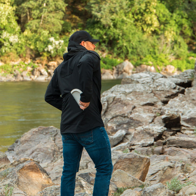A person wearing a black ODIN Disc Golf jacket with a hood, showcasing the back lower disc pocket.