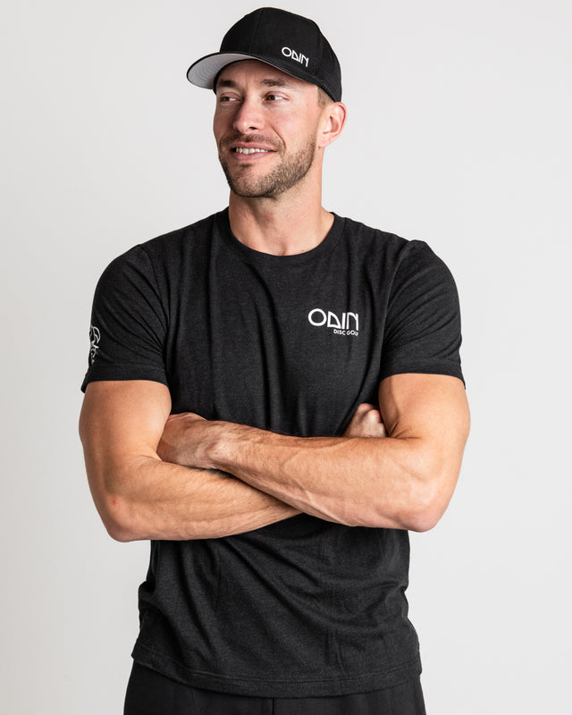 Black Men's disc golf t-shirt  front view of model, showcasing Black snapback disc golf hat with small white Odin vinyl print | Odin Disc Golf Apparel
